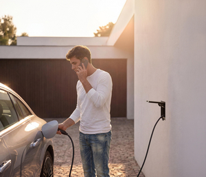 Man aan de telefoon laadt zijn wagen op via een Sotto Murra Solid laadpunt aan een witte gevel