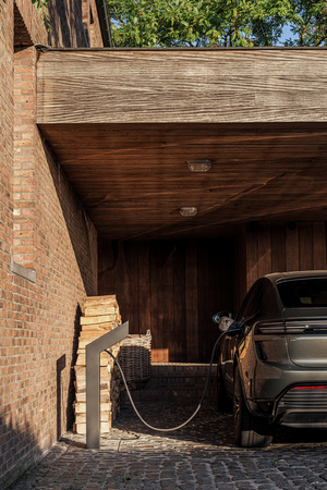 Wagen laadt op via een Sotto Terra laadpunt onder de houten carport van een bakstenen villa